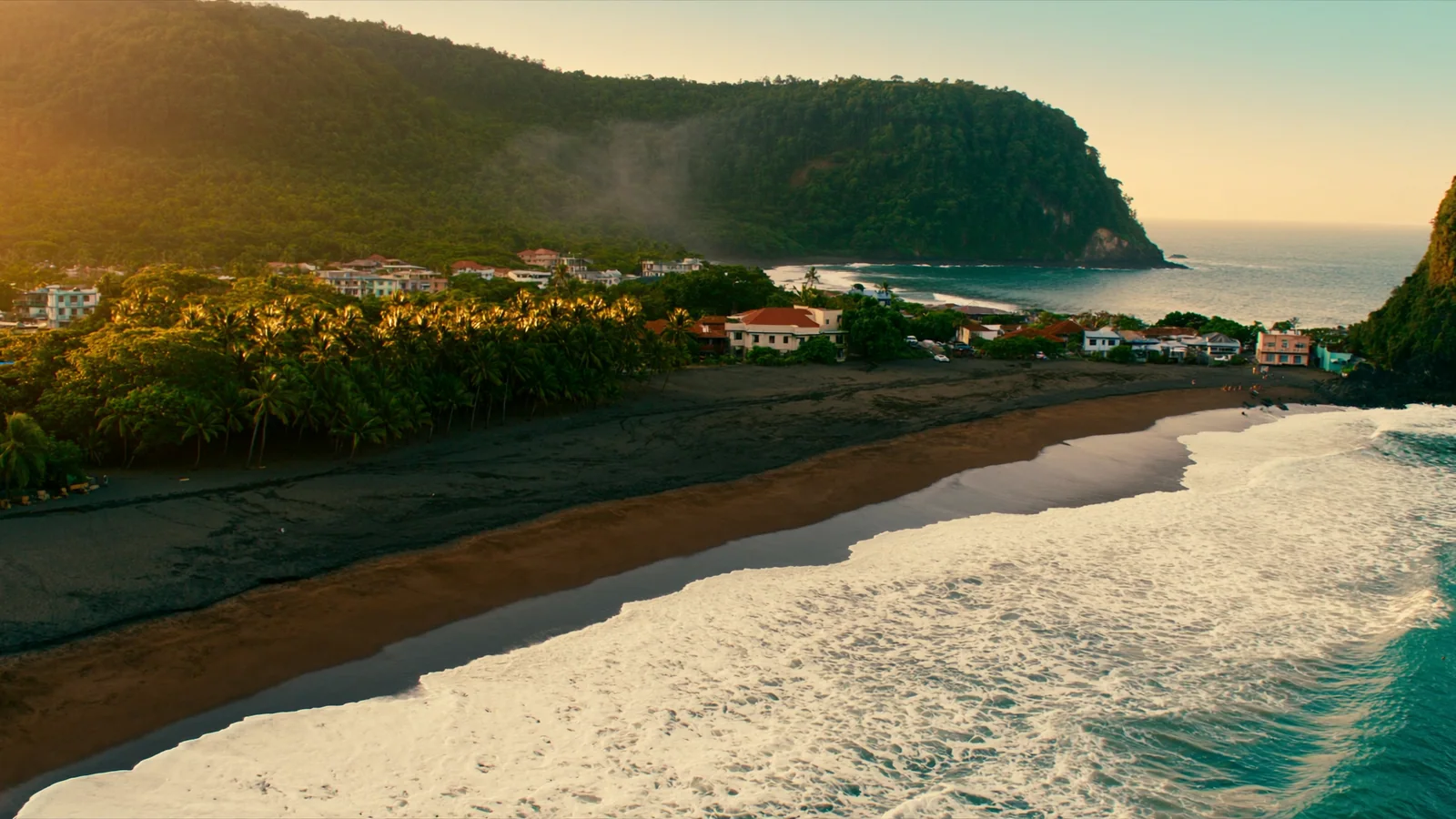 The Pacific coast at golden hour — dark sand, surf and a headland behind the town